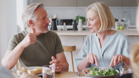 family with senior parents and adult offspring eating meal around table at home together