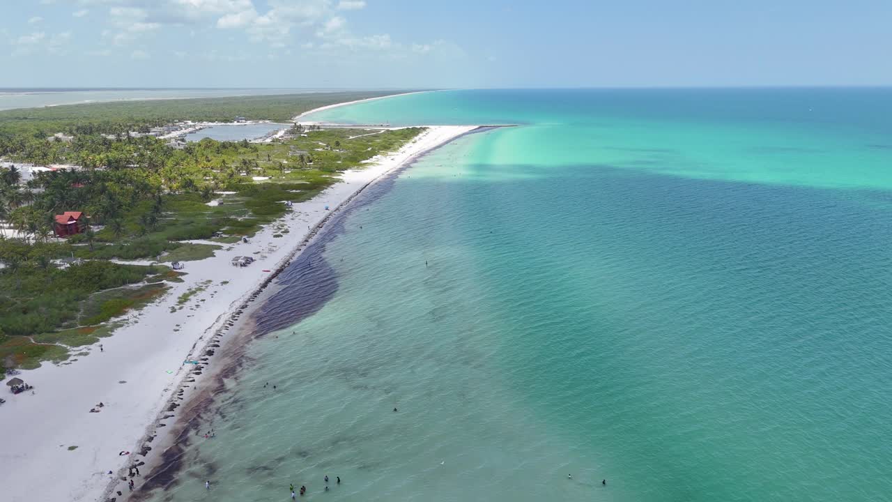 Molo che si estende nel mare turchese dei Caraibi a El Cuyo, Yucatán, Messico. Spiaggia di sabbia bianca, palme e persone che si godono una giornata tropicale e soleggiata