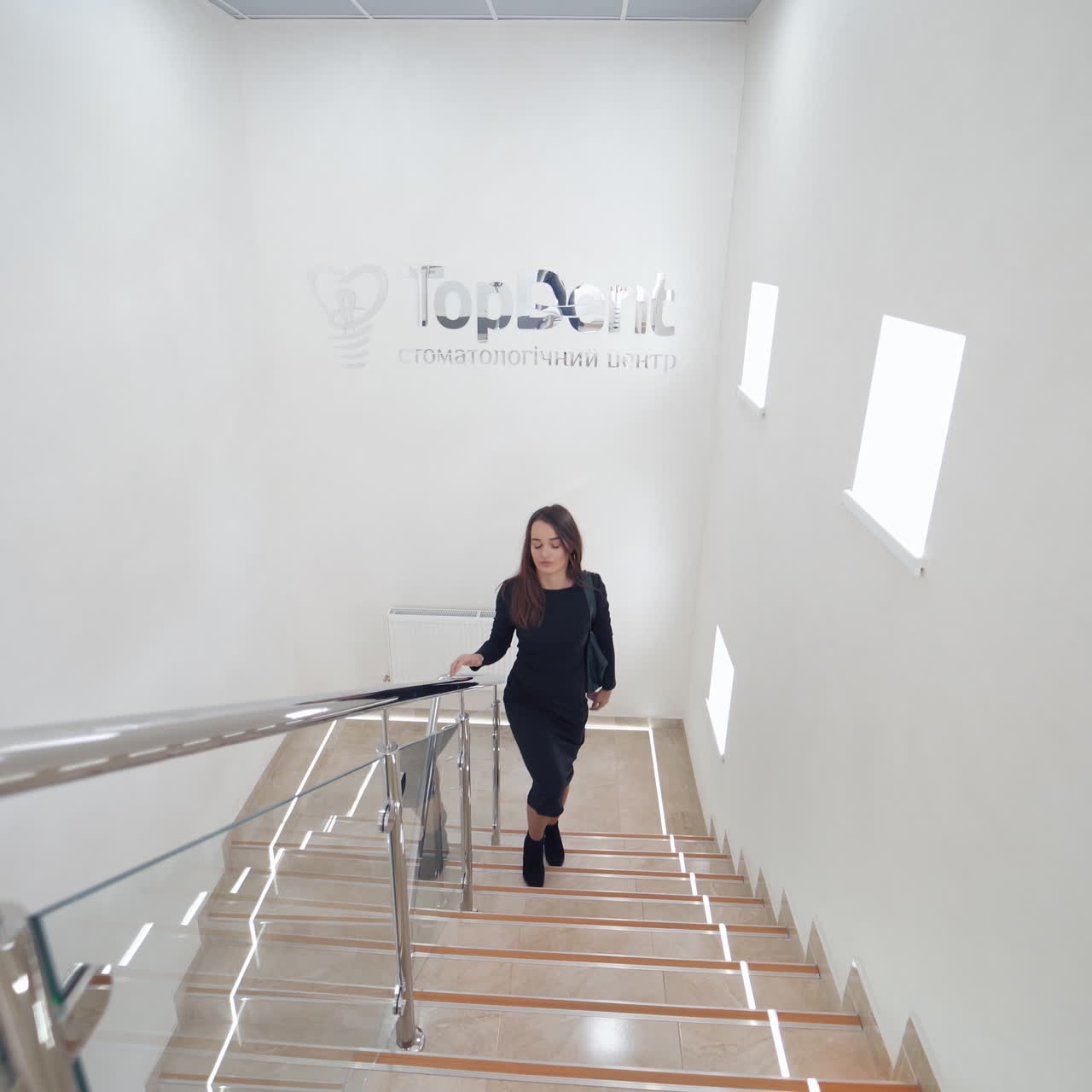 Beautiful woman in the dental centre. Young female is going upstairs inside the modern stomatology clinic. Attractive girl comes to the table of a receptionist in dental hospital.