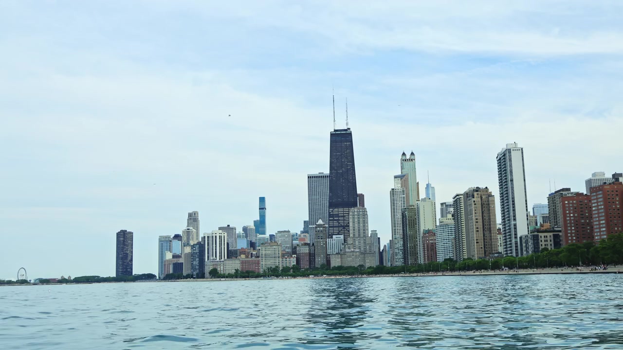 Vista dello skyline di Chicago dall'acqua con edifici, nuvole e il lago in primo piano di giorno in estate.
