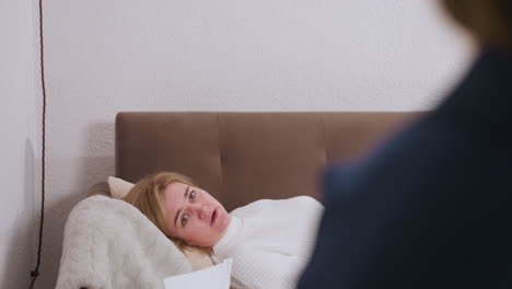 vulnerable visitor lying on sofa during therapy session wiping tears with tissue while speaking to listening partner, cozy cushions and wooden table with pencils tissue box and clock visible