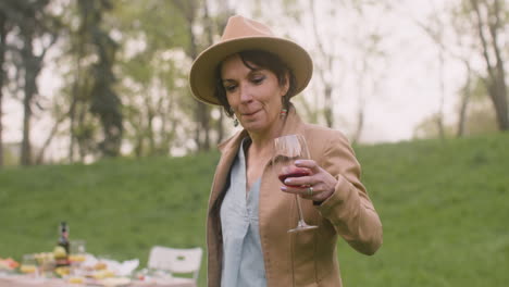 middle aged woman dancing while holding a wine glass in the park