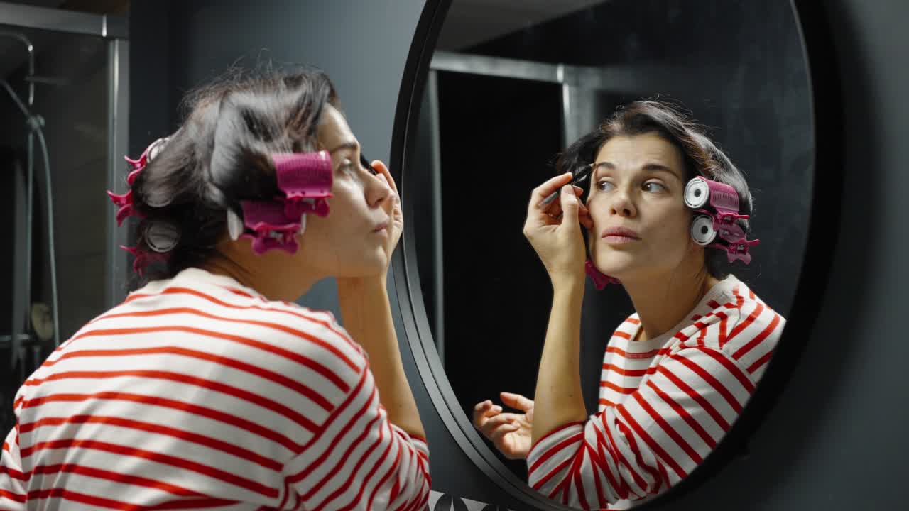 mujer mirándose en el espejo y usando un lápiz de cejas