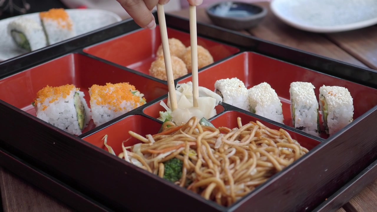 Person, die mit Essstäbchen eingelegten Ingwer aus einer Bento-Box aufnimmt