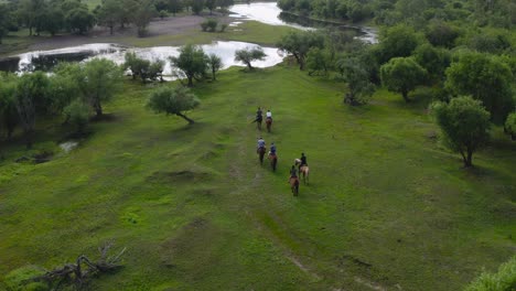 group of people riding horses in an idyllic field with ponds