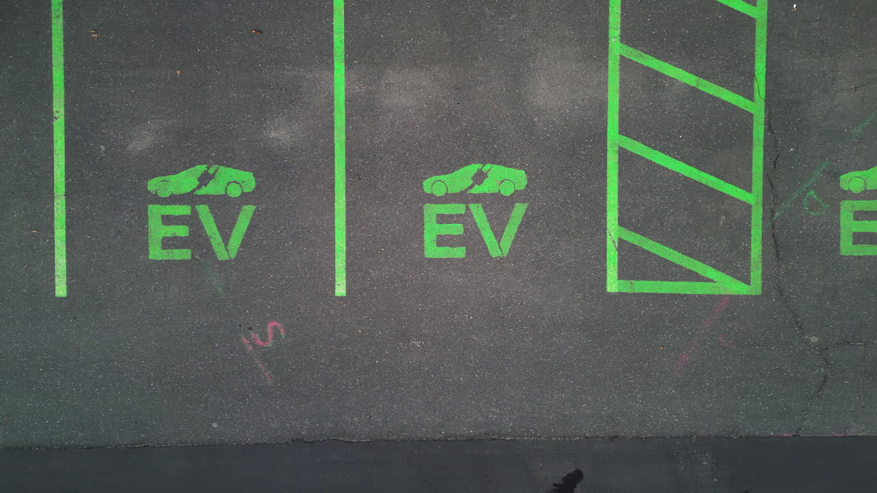 Cars and parking area with EV Electric Vehicle lots in american town. Aerial top down flyover. Modern parking area with road markings for electric cars.