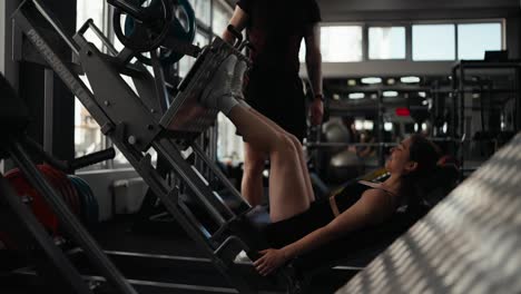 woman doing leg press with personal trainer in gym