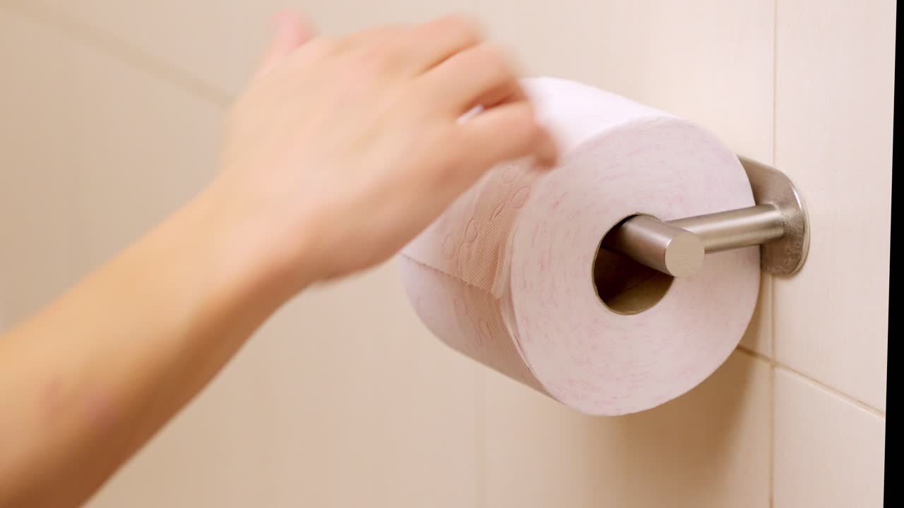 Man pulls sheets from toilet paper roll in bathroom