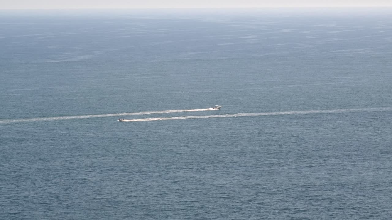 Locked-off wide shot of two speedboats leaving white trails on calm blue ocean