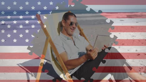 Puzzle-über-Die-Amerikanische-Flagge-Gegen-Einen-Mann,-Der-Ein-Digitales-Tablet-Benutzt-Und-Auf-Einem-Liegestuhl-Am-Strand-Sitzt