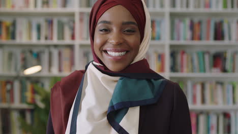 Retrato-De-Una-Joven-Y-Encantadora-Mujer-Afroamericana-Riéndose-Mirando-A-La-Cámara-Estudiante-Parada-En-La-Biblioteca