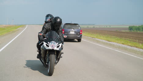 biker with girlfriend rides motorcycle along road past field