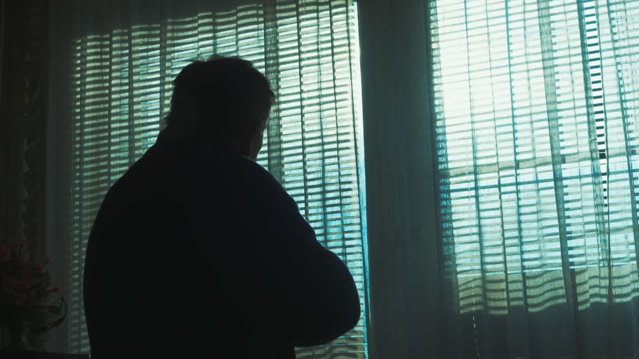 ベールのかかったカーテンの後ろに逆光のシルエットが単独で立ち、暗い部屋の中で物思いにふけっている。