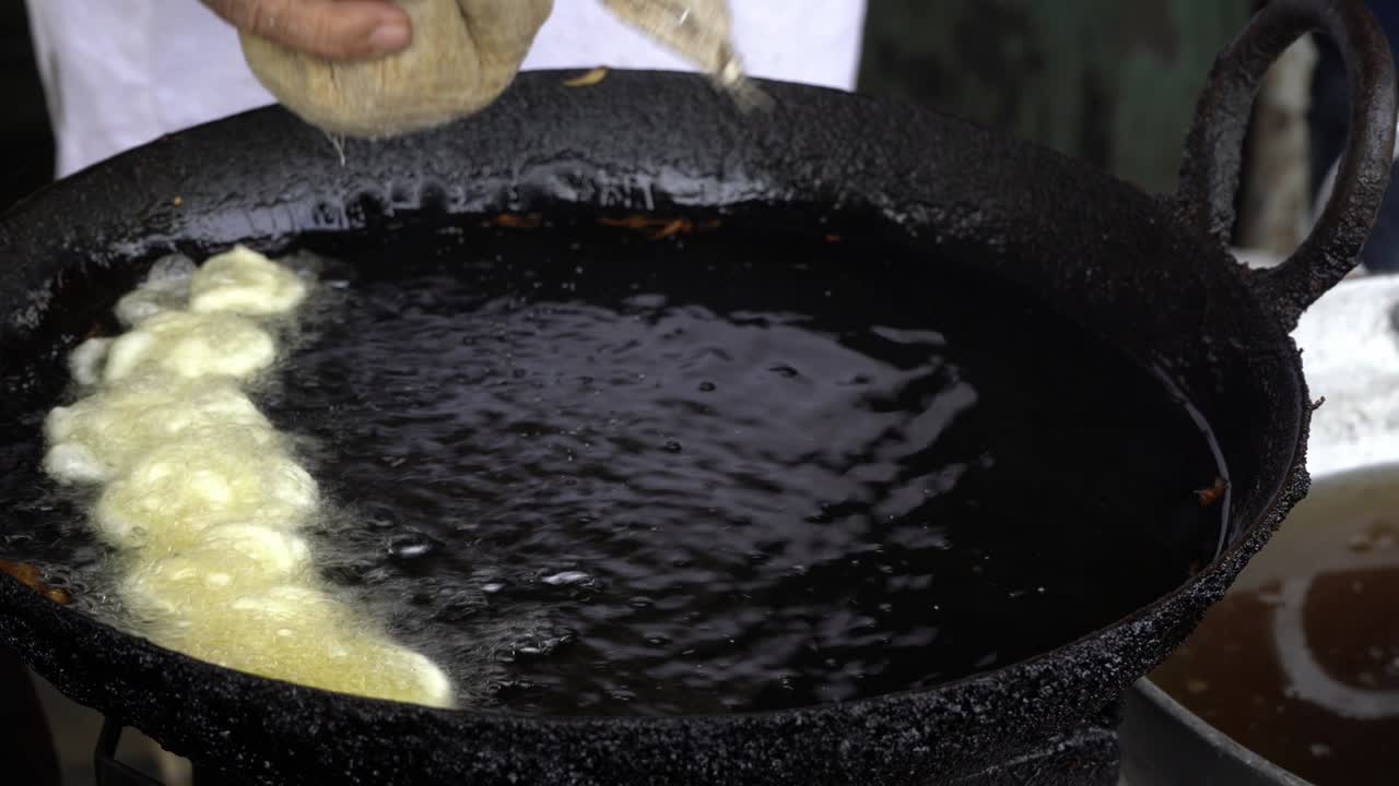Primo piano di una mano che prepara il dolce Jalebi in una grande padella d'olio, India