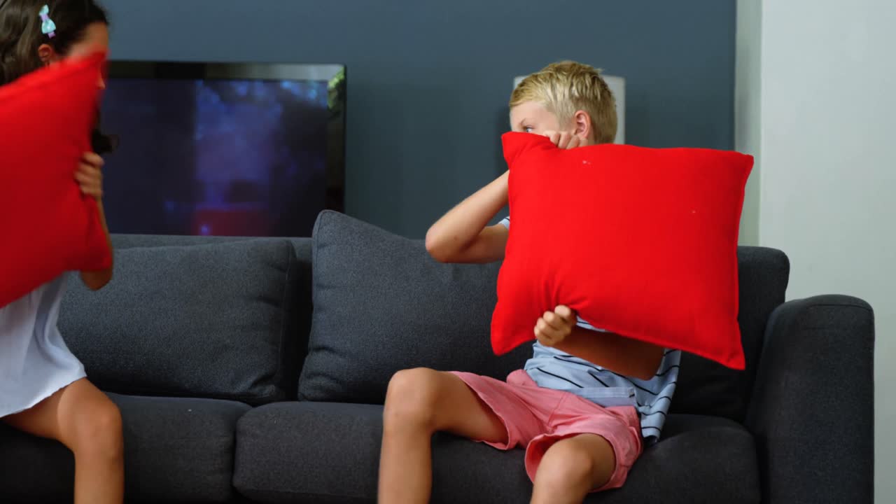 hermanos luchando con almohadas en la sala de estar