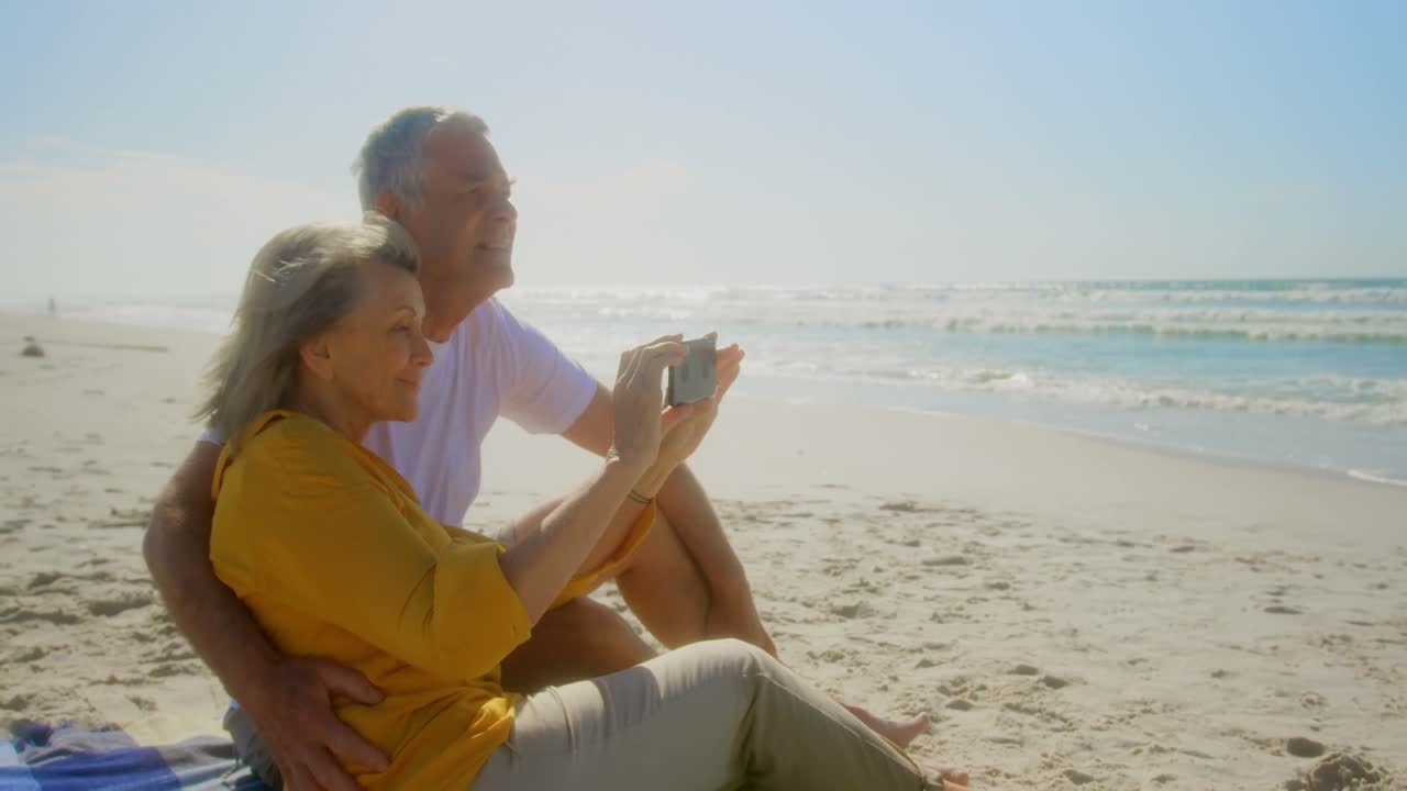 Vista lateral de pareja caucásica de edad avanzada activa tomando fotos en la playa 4k