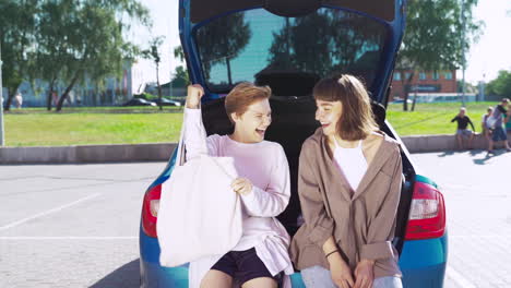 two women friends are happy looking at a bag in the car trunk