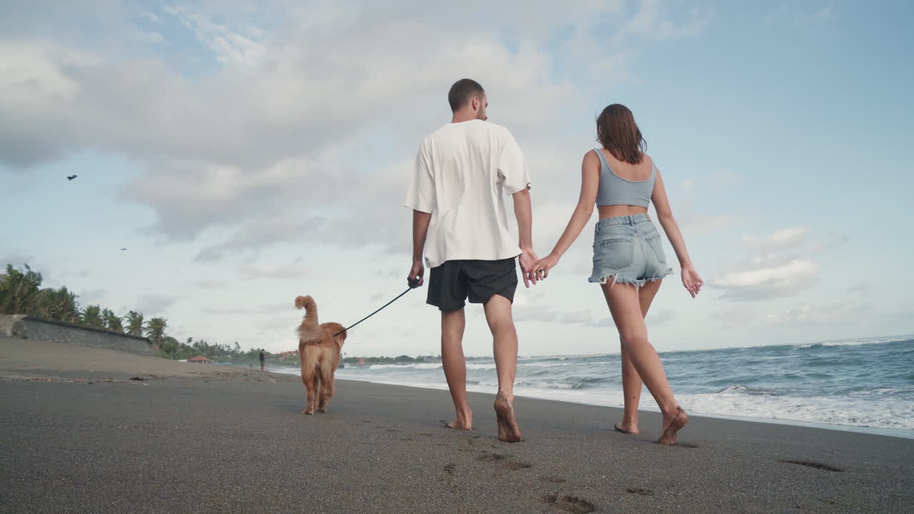 una pareja de jóvenes paseando con un perro a lo largo del océano.