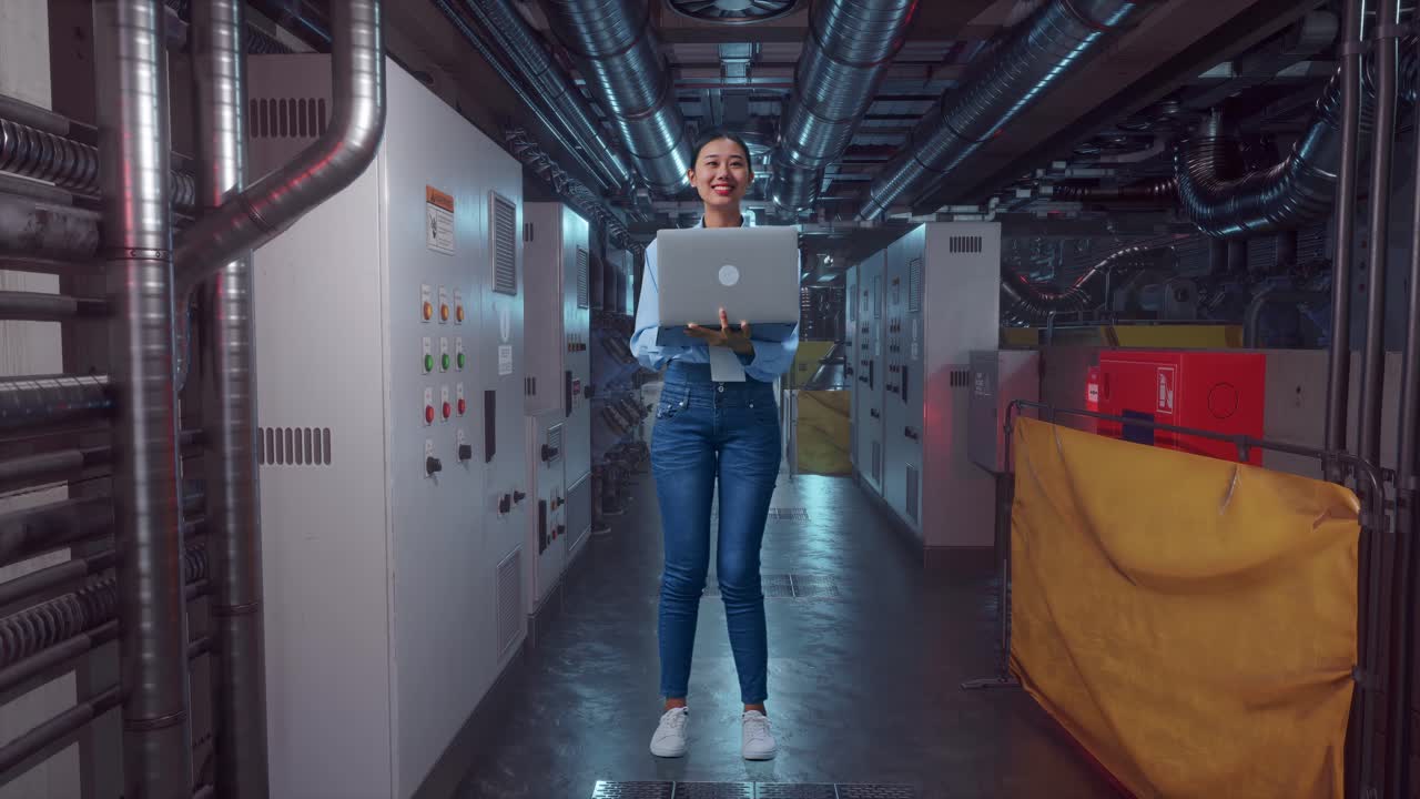 Full Body Of An Asian Female Worker Standing With Her Laptop In Engine Control Room, She Observes By Looking Around Before She Come To Concentrating With Her Laptop