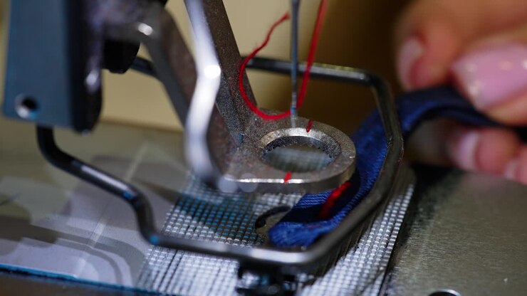 Sewing machine in motion. Tailor puts cloth under a sewing machine. Needle of a sewing machine makes a thread stitch. Macro shot.