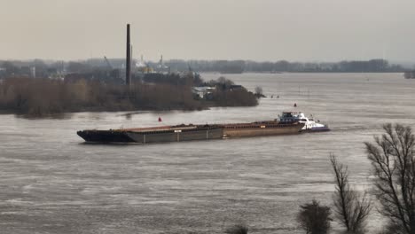 aerial close up of a tug pushing a barge down the flooded waal river near slot loevestein, gorinchem netherlands in the winter of 2024 after heavy rains fall over northern europe