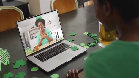 Smiling-african-american-woman-with-beer-wearing-band-with-clovers-on-video-call-on-laptop