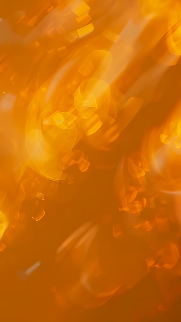 Vertical video: Closeup initiating glowing amber particles drifting outward, featuring bokeh shapes