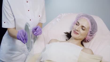 a beautician takes a mirror in her hands and shows the result of the procedure for lip augmentation for the client at the cosmetology center. a woman looks on her lips after injections of botox in the reflection.