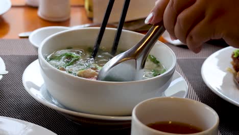 person eating noodle soup with chopsticks and spoon