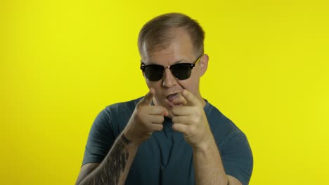 Portrait-of-young-man-posing-in-t-shirt.-Cool-handsome-guy-wears-sunglasses,-point-fingers-at-camera
