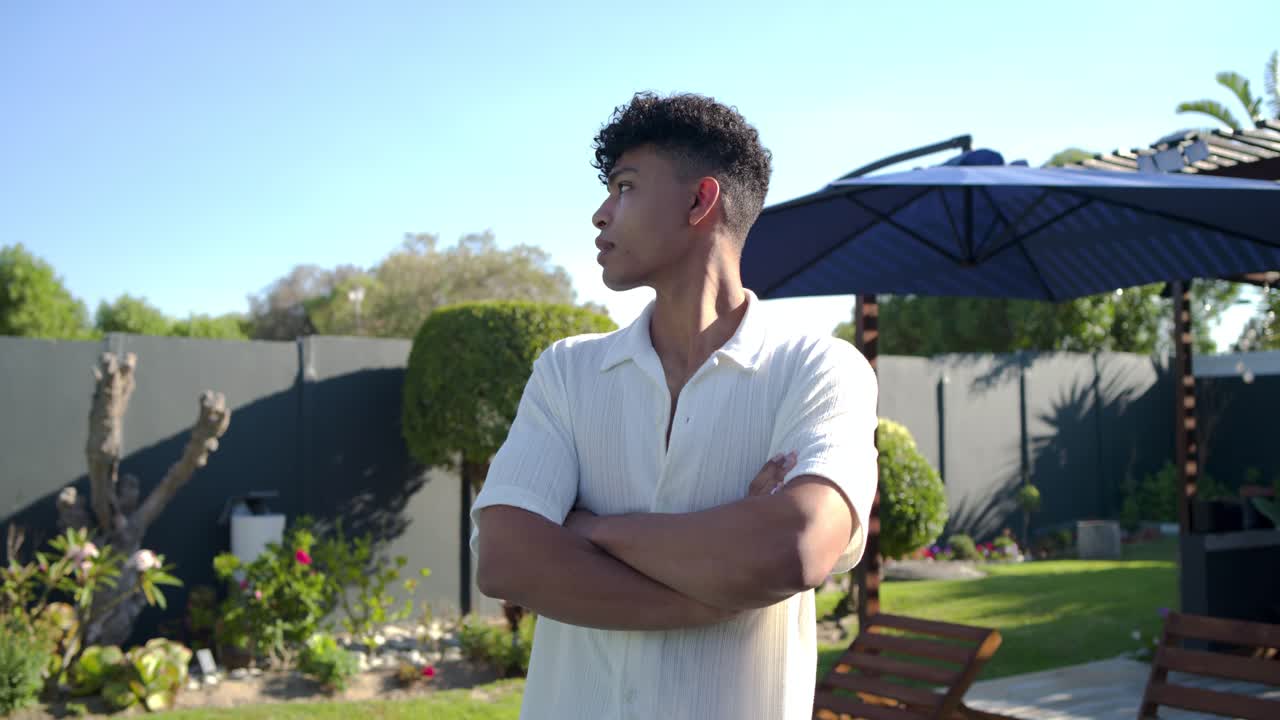 Uomo afroamericano sui 20 anni con una camicia bianca che, notando un movimento fuori campo, si gira sorridendo e posando vicino a un ombrello.