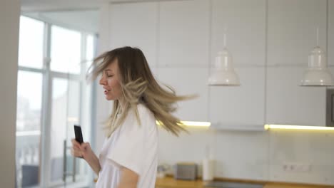 Funny-playful-blonde-woman-dancing-and-singing-at-home-having-fun,-use-remote-controller-as-a-microphone