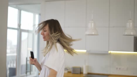 mujer rubia divertida juguetona bailando y cantando en casa divirtiéndose, usar el control remoto como un micrófono