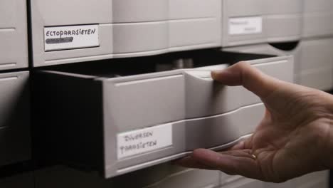 a hand opens a labeled drawer in a medical archive marked for ectoparasites and various parasites, revealing organized storage.