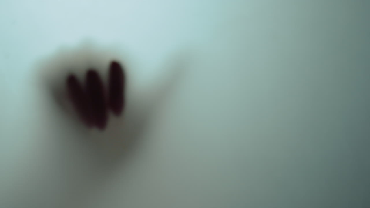 Macro video of one female hand moving behind frosty glass. Hand shadow.