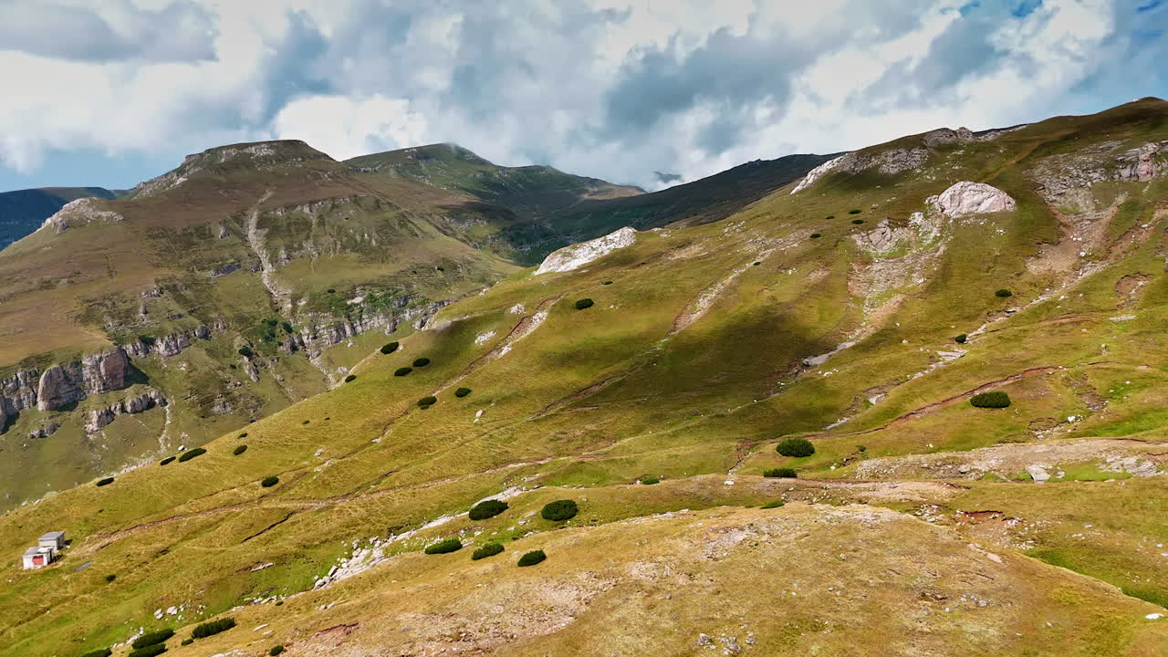 Mountain landscape under a cloudy sky. Rolling hills covered in grass lead to majestic mountains under a partly cloudy sky, creating a serene natural view
