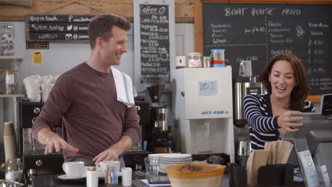 couple behind the counter at a cafe talk as they work