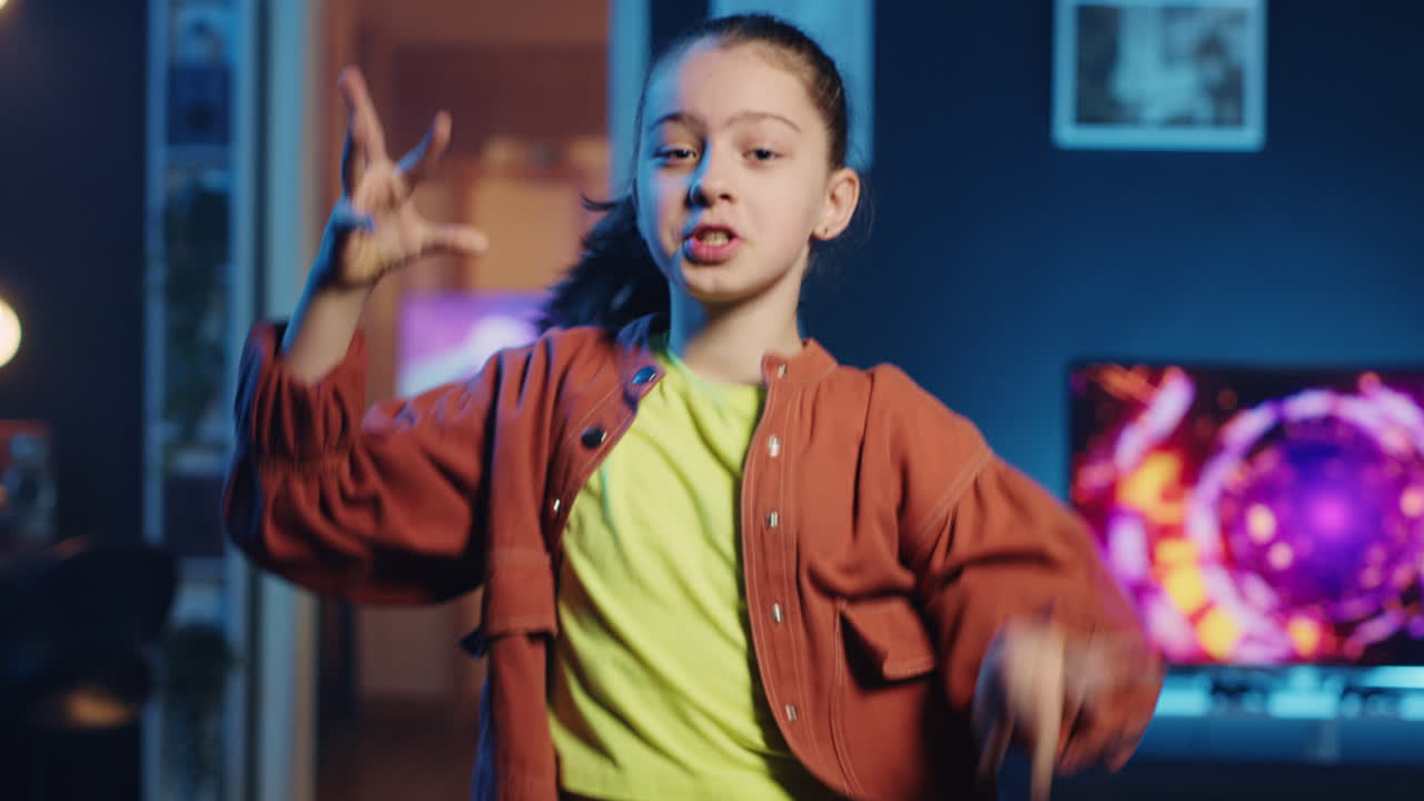Pretty little girl dancing and singing while shooting video for social media platform at home