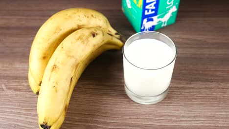 Pouring-milk-in-a-glass-and-banana-on-table-,