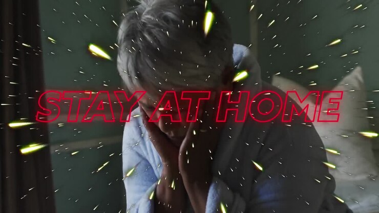 Stay at home neon text and light trails against stressed african american woman sitting on bed