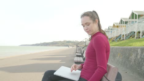 Junge-Frau-Schaltet-Ihr-Telefon-Aus-Und-öffnet-Ihren-Laptop-Entspannt-Und-Arbeitet-Am-Strand