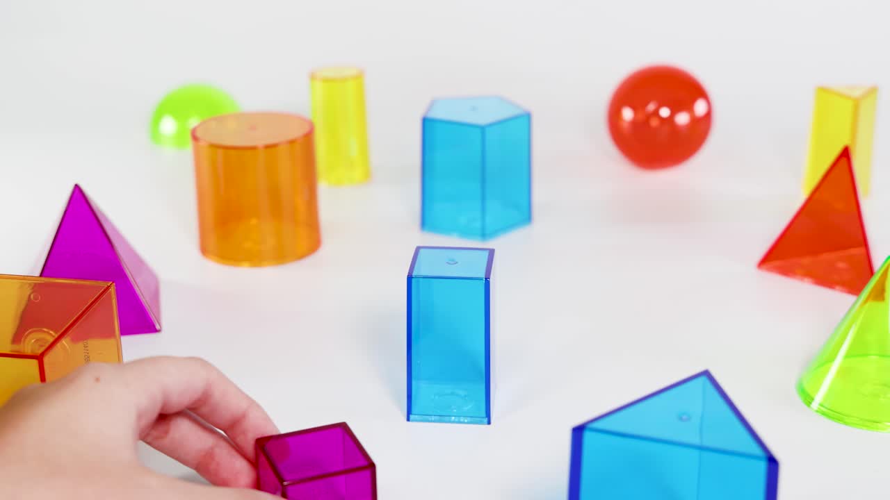 A child's hands stack colorful geometric shapes on a white surface, exploring balance and form in bright lighting