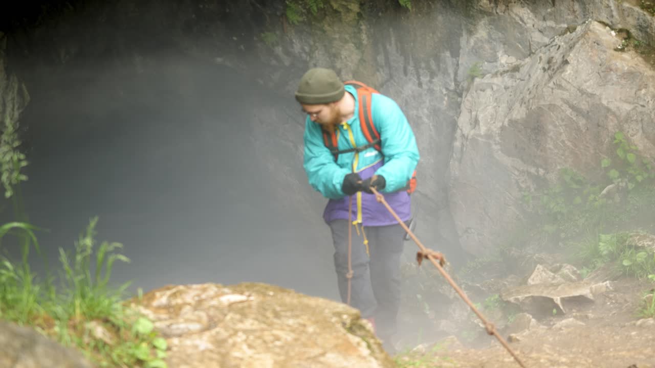 hombre bajando en rappel por la entrada de una cueva de niebla