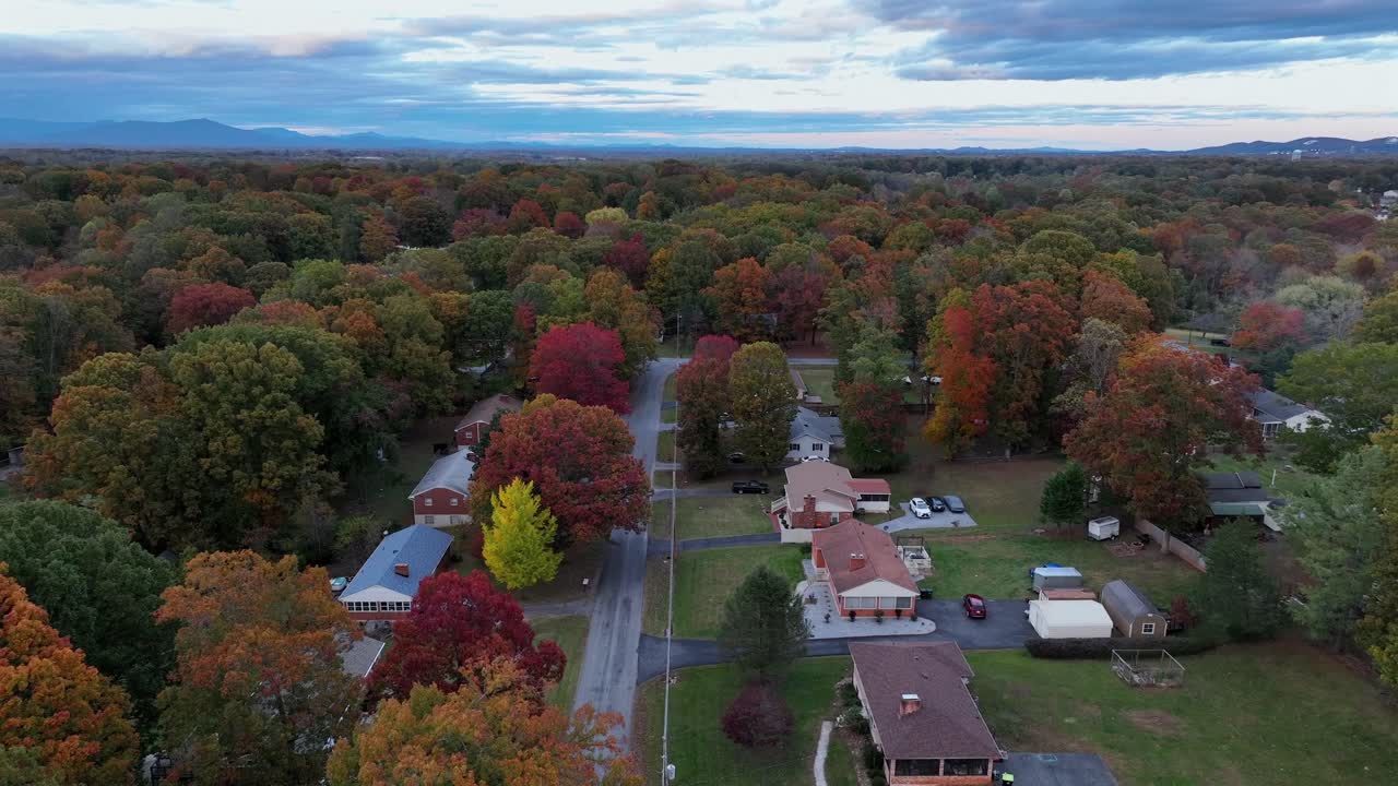 Aerial view of an American suburban neighborhood in peak autumn, showing colorful fall foliage, quiet residential streets and peaceful homes surrounded by vibrant trees. Wide shot. Quiet scene