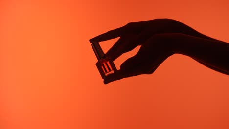 Elegant Display of Nail Polish Bottle against Deep in Silhouette a Hand Gracefully Holds a Bottle of Nail Polish Silhouetted against a Deep Orange Background Emphasizing Elegance
