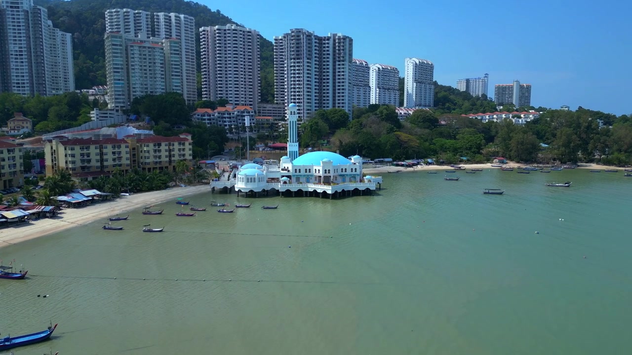 Malezya, Penang, Tanjung Bungah'taki yüzen cami, kıyı boyunca geleneksel balıkçı tekneleri ve arka planda modern binalar. Muhteşem havadan görünüm, ileri doğru uçan panoramik drone görüntüsü.