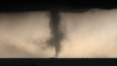 scary tornado spinning below dark storm clouds with heavy rain and hail falling