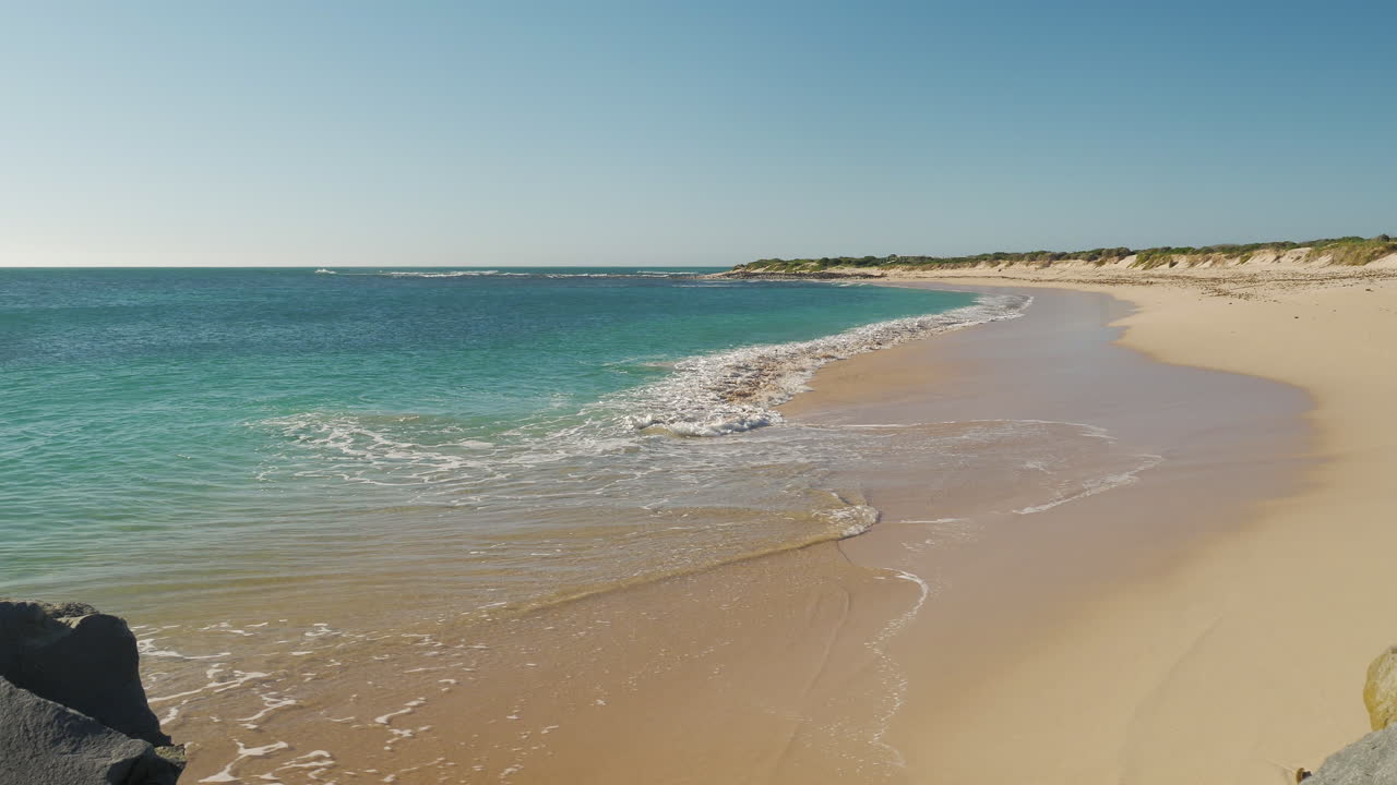 Piccole onde che lambiscono una bellissima e deserta spiaggia sabbiosa, giornata di sole.