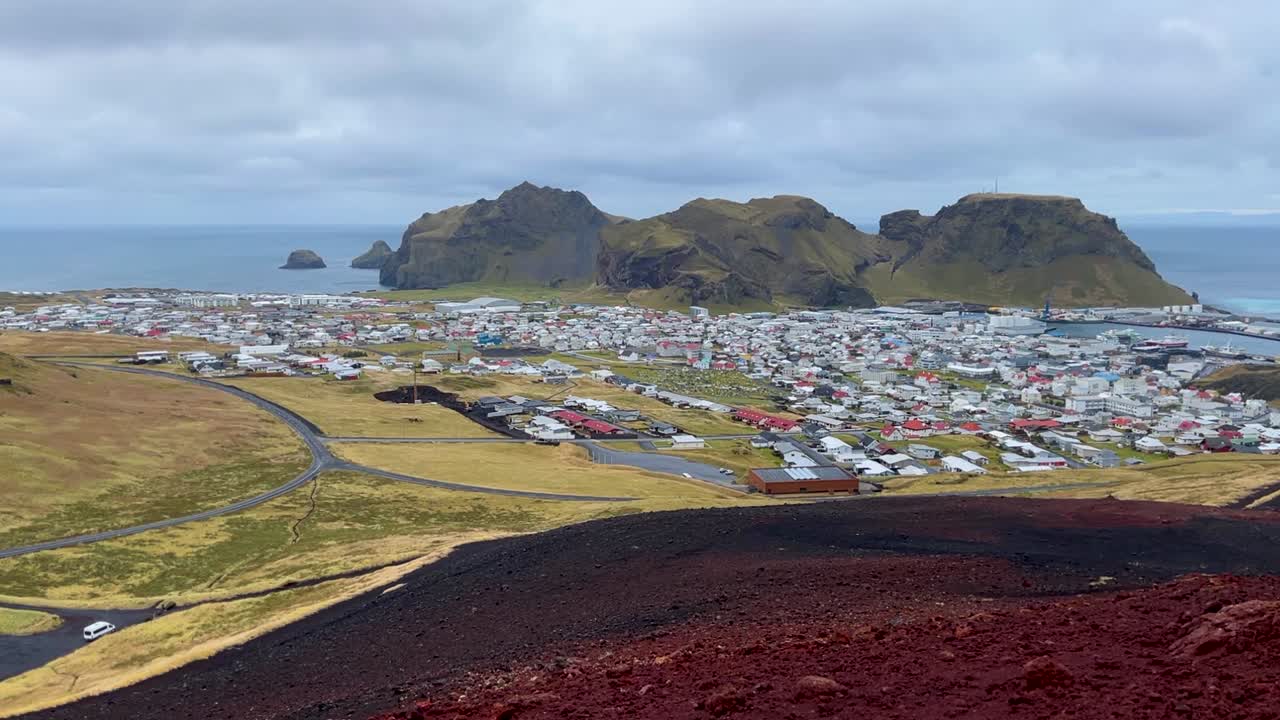 Red Rock Foreground Of Eldfell Volcano Near Vestmannaeyjabær Town At Heimaey, Iceland. Wide Shot
