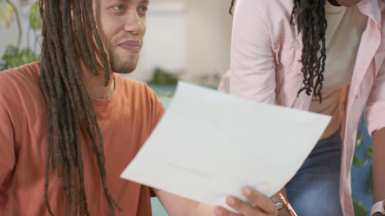 African colleagues high-fiving as woman approaching right, reviewing charts and marking at table